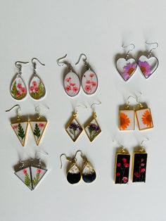 nine pairs of earrings with flowers and hearts hanging from the ear hooks on a white surface