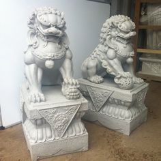 two stone lions sitting on top of each other in front of a white wall and floor