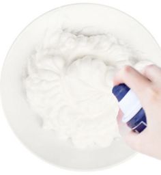 a hand is spraying cream on a white plate