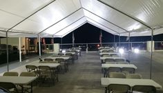 tables and chairs are set up under a large white tent with lights on the roof