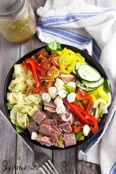 a salad with meat and vegetables in a black bowl on a white table cloth next to a glass of water