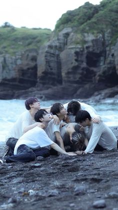 group of young men huddled together on the beach with water in the backgroud