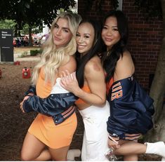 three beautiful women standing next to each other in front of a brick wall and tree