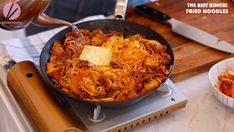 a pan filled with food sitting on top of a stove next to a bowl of noodles