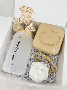 an open box with personalized items in it, including a gold bracelet and white rose