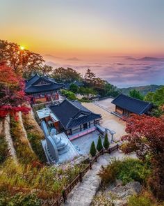 the sun is setting over some buildings on top of a hill with mountains in the background