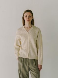 The person in the photograph is wearing a cardigan with a deep V-neckline, which gives it a relaxed and comfortable feel. The cardigan showcases cable knit details along the front, adding a classic and textural element to the design. It features a button-down front with small, subtle buttons that blend into the overall color scheme. The ribbed cuffs and hem offer a snug fit, and the cardigan seems to be made from a material that provides warmth and softness.- The cable knit design creates a timeless aesthetic, indicating that this garment could be a staple in a classic wardrobe.- The V-neckline is versatile, allowing the garment to be styled over various types of clothing, from collared shirts to simple tees.- The neutral color of the cardigan suggests that it could be easily paired with o V-neck Cable Knit Outerwear For Layering, Elegant V-neck Cable Knit Outerwear, Beige Cable Knit V-neck Cardigan, Beige V-neck Cable Knit Cardigan, Elegant Cable Knit V-neck Sweater For Fall, Classic Cable Knit Cardigan For Work, Cable Knit V-neck Outerwear For Layering, Chic Cable Knit V-neck Cardigan, Classic Beige Cable Knit Cardigan