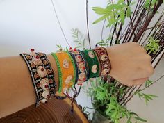 a woman's arm with bracelets on it and a plant in the background