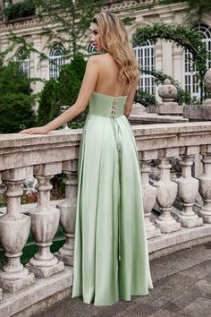 a woman in a long green dress standing on a stone wall with her back to the camera