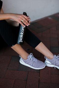 a woman sitting on the ground with her feet propped up holding a water bottle in one hand