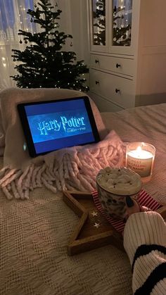 a tablet sitting on top of a bed next to a christmas tree with candles in front of it