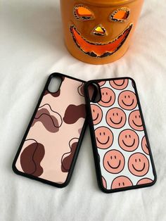 two iphone cases with faces on them sitting next to a potted plant and pumpkin