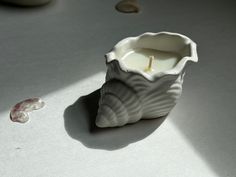 a small white candle sitting on top of a table next to a shell shaped object