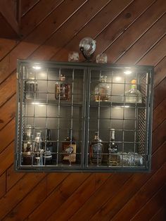 a glass cabinet with liquor bottles and glasses on the shelves in front of wooden walls