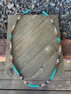 a necklace with beads and stones on a wooden table next to some rocks in the background