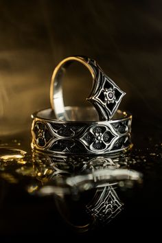 two wedding rings sitting next to each other on top of a reflective surface in the dark