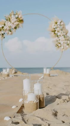 two vases filled with white flowers sitting on top of a sandy beach