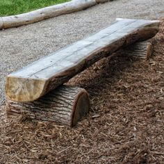 a wooden bench sitting on top of a pile of mulch next to a tree