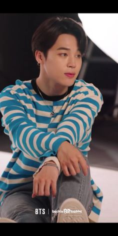 the young man is sitting down with his hand on his hip and wearing a striped shirt