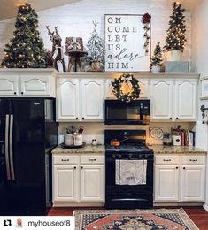 a kitchen decorated for christmas with white cabinets, black appliances and trees on the wall