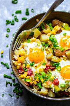 a bowl filled with fried eggs and vegetables next to a fork on top of a table