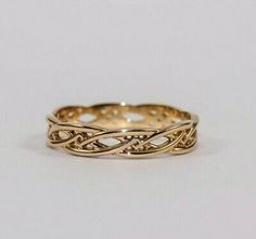 a gold wedding band with intricate designs on the sides and an intertwined design in the middle