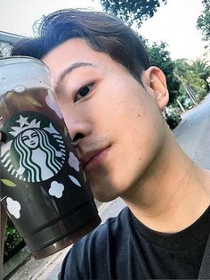 a young man holding up a starbucks cup to his face and looking at the camera