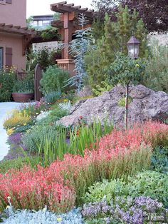 a garden with lots of flowers and rocks in the foreground, next to a house