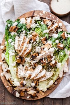 a salad with chicken, lettuce and parmesan cheese on a wooden plate