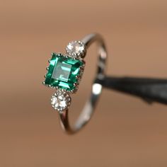 It is a real lab emerald ring. The main stone is 6 mm*6mm square cut lab emerald, weight about 0.92 carats. The basic metal is sterling silver and plated with rhodium. To change the metal to a solid gold (white/rose) or platinum is also available, please ask for a quotation if you want. You can also go to my shop Home for more elegant rings: https://www.etsy.com/shop/godjewelry?ref=hdr_shop_menu Emerald is May birthstone. More emerald rings: https://www.etsy.com/shop/godjewelry?ref=hdr_shop_menu Elegant Sterling Silver Emerald Three Stone Ring, Silver Asscher Cut Emerald Jewelry, Classic Jewelry With May Birthstone In Princess Cut, Classic Jewelry With Princess Cut May Birthstone, Square Cut Diamond Jewelry For May Birthstone, Classic Jewelry Princess Cut May Birthstone, Classic May Birthstone Jewelry With Princess Cut, Classic Princess Cut May Birthstone Jewelry, Silver Emerald Jewelry With Square Cut