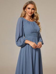 a woman wearing a blue dress with long sleeves and pleaed details on the shoulders