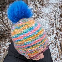 a woman wearing a multicolored knitted hat with a blue pom - pom