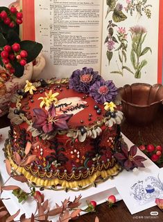 a decorated cake sitting on top of a table next to an open book and potted plant