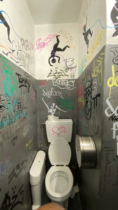 a bathroom with graffiti on the walls and a toilet in the middle, next to a trash can