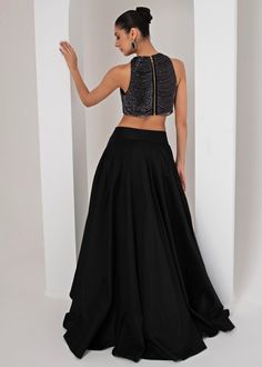 Introducing the stunning Black High Low Skirt with Nalki Blouse, crafted from luxurious taffeta silk. The black nalki blouse boasts a chic, sleeveless halter neck design, adorned with intricate halo nalki chain embellishments that add a touch of shimmer and sophistication. Paired perfectly with a flowing, solid black high-low skirt, creating an ensemble that effortlessly merges modern elegance with traditional charm. Ideal for Cocktails, Sangeet nights, or evening parties, this outfit is designed to make you stand out with its sleek silhouette and striking contrast. Composition : Skirt, Blouse - Taffeta Silk Care: Dry Clean Only and Vacuum Storage This product can be customized for sleeves, blouse length and neckline Delivery : 4-6 weeks as the product is hand crafted. Check Size Guide or Fitted Silk Lehenga, Sleeveless Silk Dress For Party Wear, Elegant Sleeveless Embellished Lehenga, Sleeveless Lehenga For Party, Party Wear Long Skirt, Silk Festive Evening Skirt, Silk Black Party Skirt, Silk Lehenga For Party, Satin Dress With Flared Skirt For Party