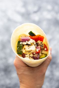 a person holding up a small bowl filled with different types of vegetables and meats