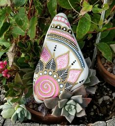 a painted rock sitting on top of a flower pot next to succulents