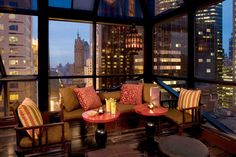 a living room filled with furniture and tall buildings in the background at night, lit up by candles