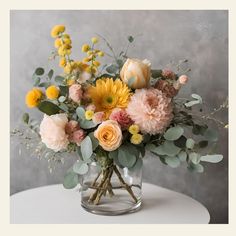 a vase filled with flowers and greenery on top of a white table next to a gray wall