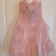 a pink dress hanging on a door with buttons and ruffles around the skirt