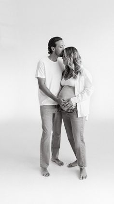 a pregnant couple kissing while standing in front of a white background with their arms around each other