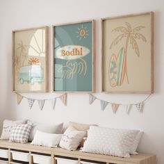 three framed pictures hang on the wall above a wooden bench with pillows and blankets underneath them