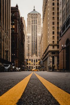 an empty city street with tall buildings in the backgroung and yellow lines painted on the road