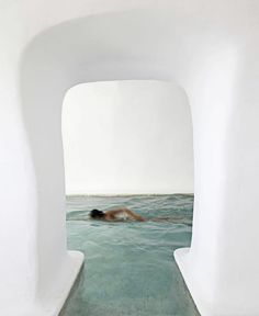 a man swims in the ocean through an arch shaped passageway that leads to another room