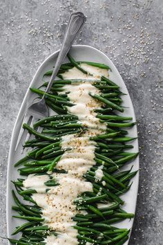 green beans with white sauce and sprinkles are on a plate next to a fork