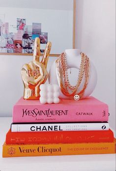 three books stacked on top of each other in front of a mirror and gold jewelry