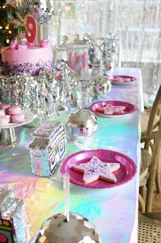 a table topped with pink and purple plates covered in frosted cookies next to a cake