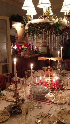 a dining room table is set for christmas dinner with candles and dishes on the table