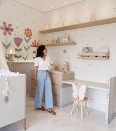 a woman standing in front of a desk with flowers painted on the wall behind it