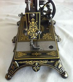 an old fashioned sewing machine sitting on top of a white sheet covered tablecloth with gold and black designs